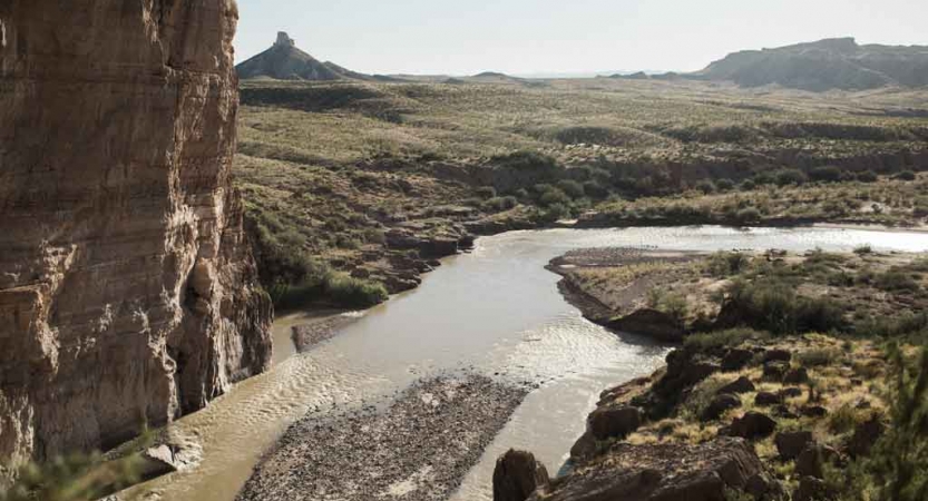 a river winds through a desert landscape with high canyon walls and mountains in the distance